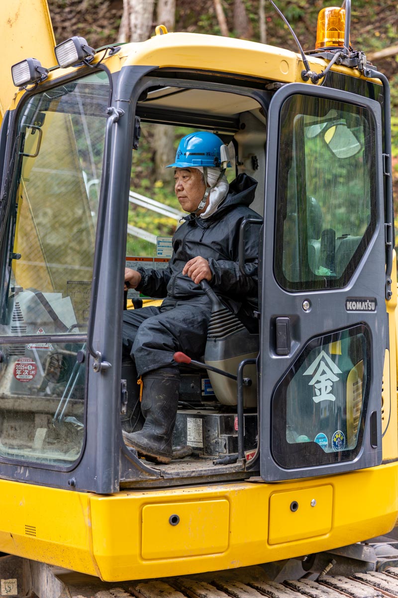 道路工事現場で白いヘルメットとオレンジ色の安全ベストを着た現場監督が、完成したばかりのアスファルト道路を確認している様子